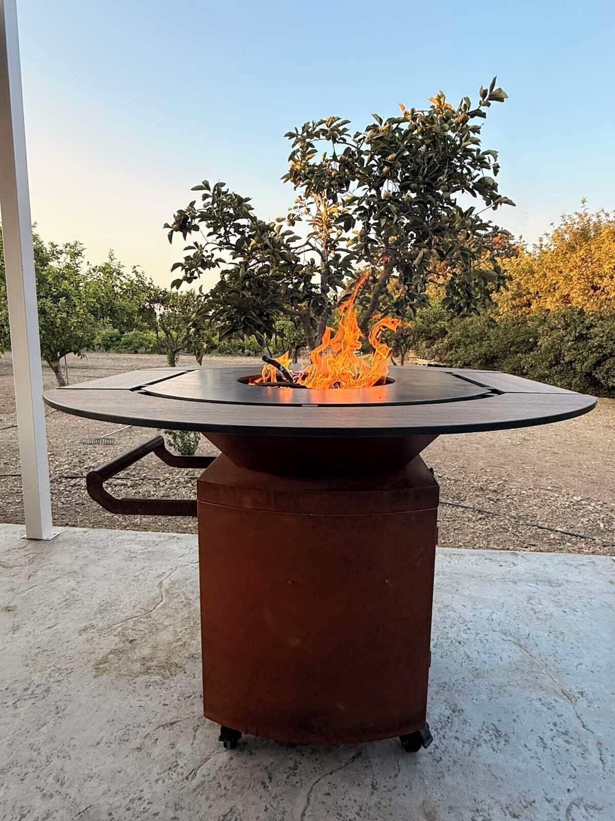 Un brasero portátil con base circular y tapa plana, rodeado de un suelo de hormigón y una estructura metálica.