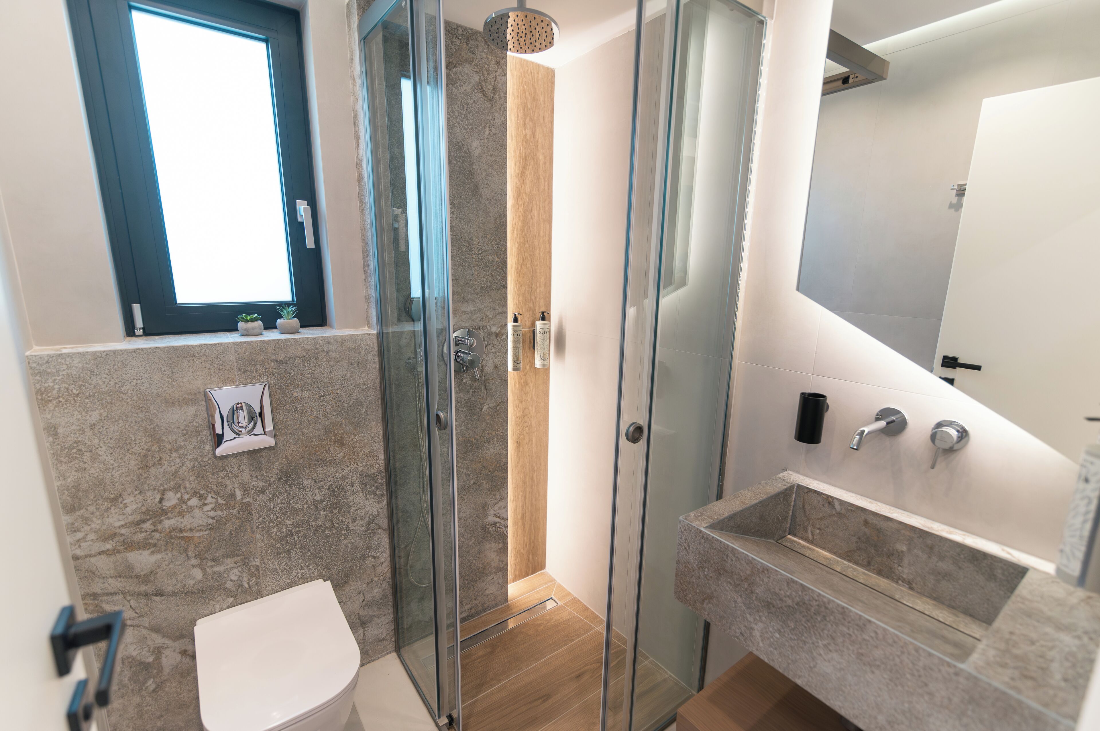 Une salle de bain moderne avec une douche à parois de verre, des toilettes, un lavabo et une petite fenêtre.