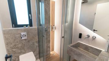 Une salle de bain moderne avec une douche à parois de verre, des toilettes, un lavabo et une petite fenêtre.