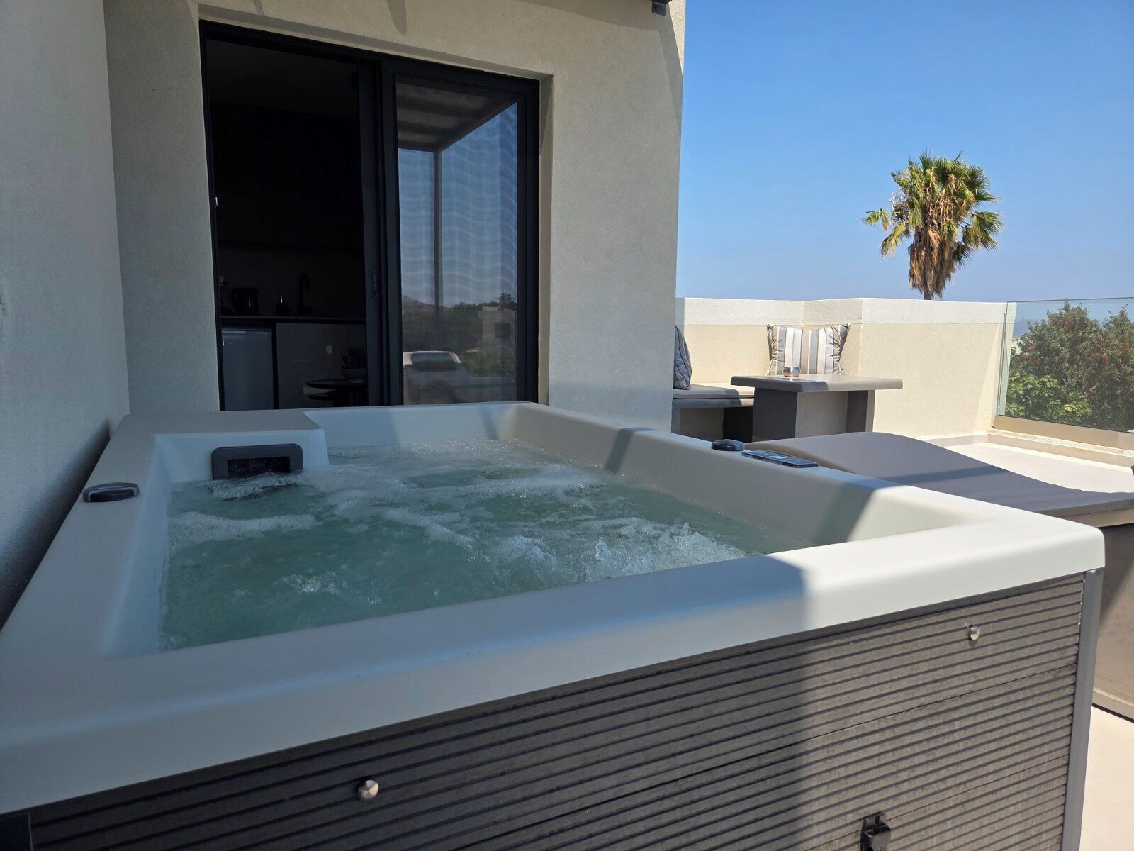 A hot tub on a balcony with a view of palm trees and a building in the background.