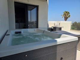Un jacuzzi en un balcón con vista a palmeras y un edificio al fondo.