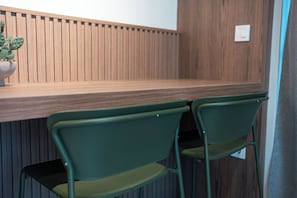 A wooden counter with a potted cactus, two green chairs, and a wooden wall with vertical slats. - Avli Residences (Kos)
