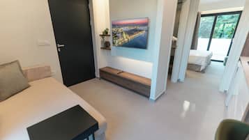 A modern hotel room with a bed, a TV mounted on the wall, a small shelf with plants, and a view of a cityscape through a window.