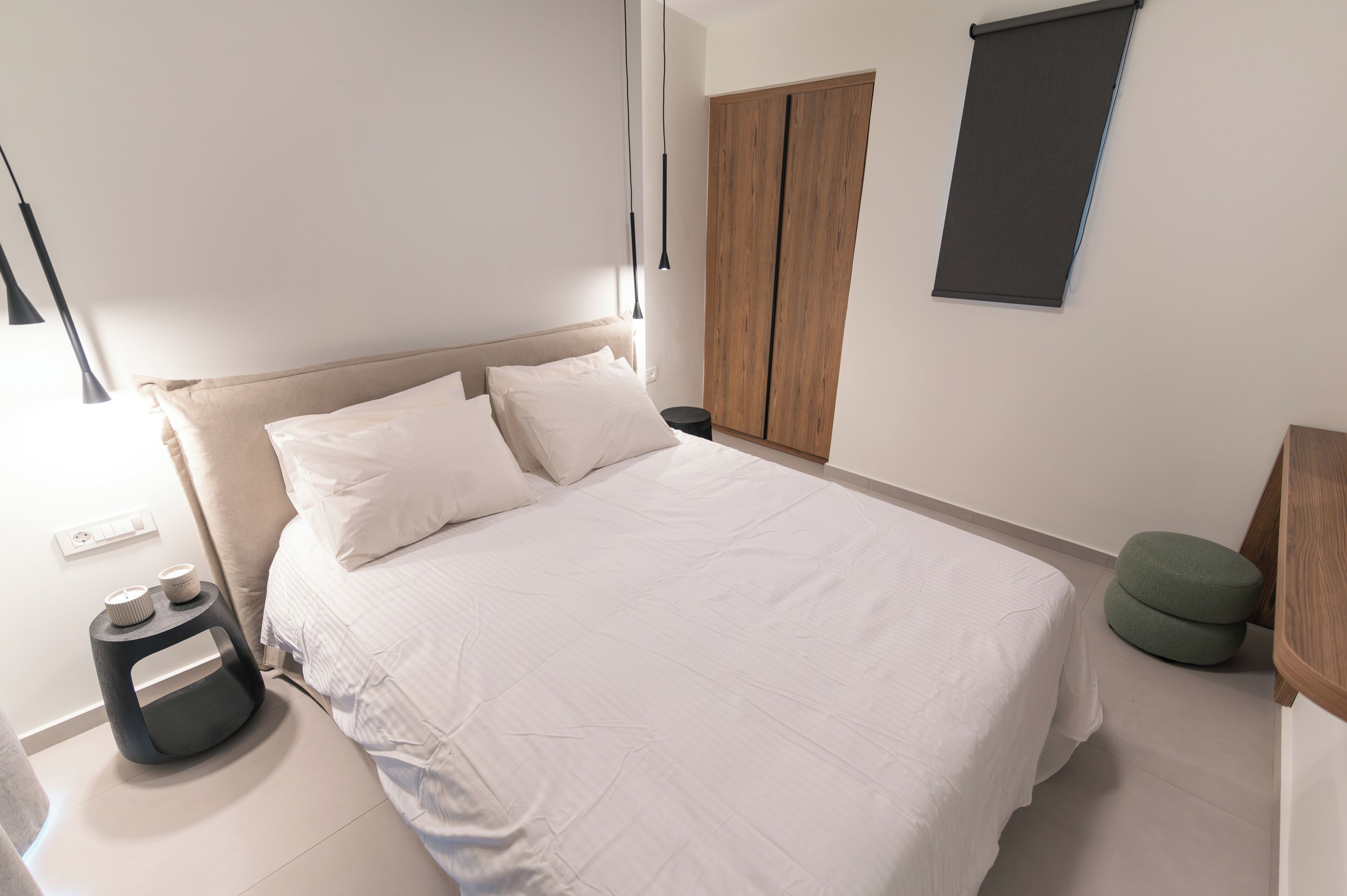 Una cama bien tendida con sábanas blancas, una mesita de noche con lámpara y un reposapiés verde.