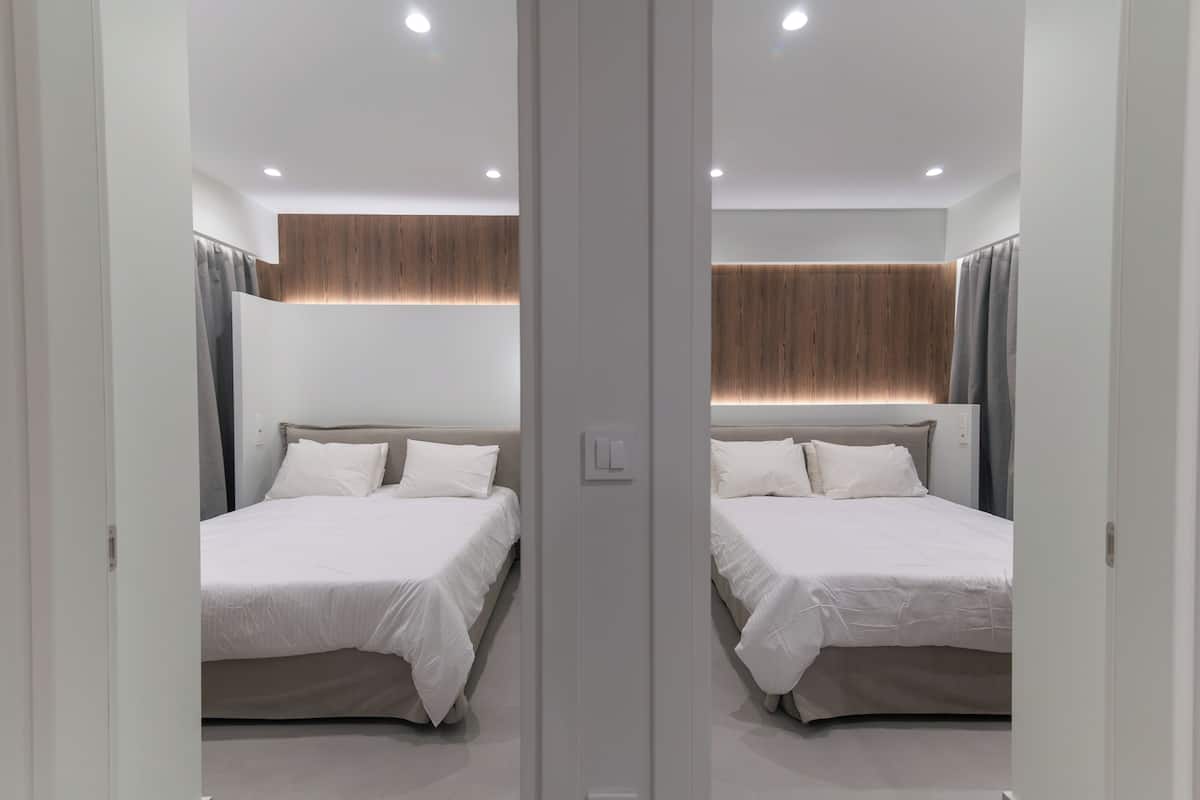 Een kamer met spiegels, twee bedden, een wand van houten panelen en een lichtschakelaar.