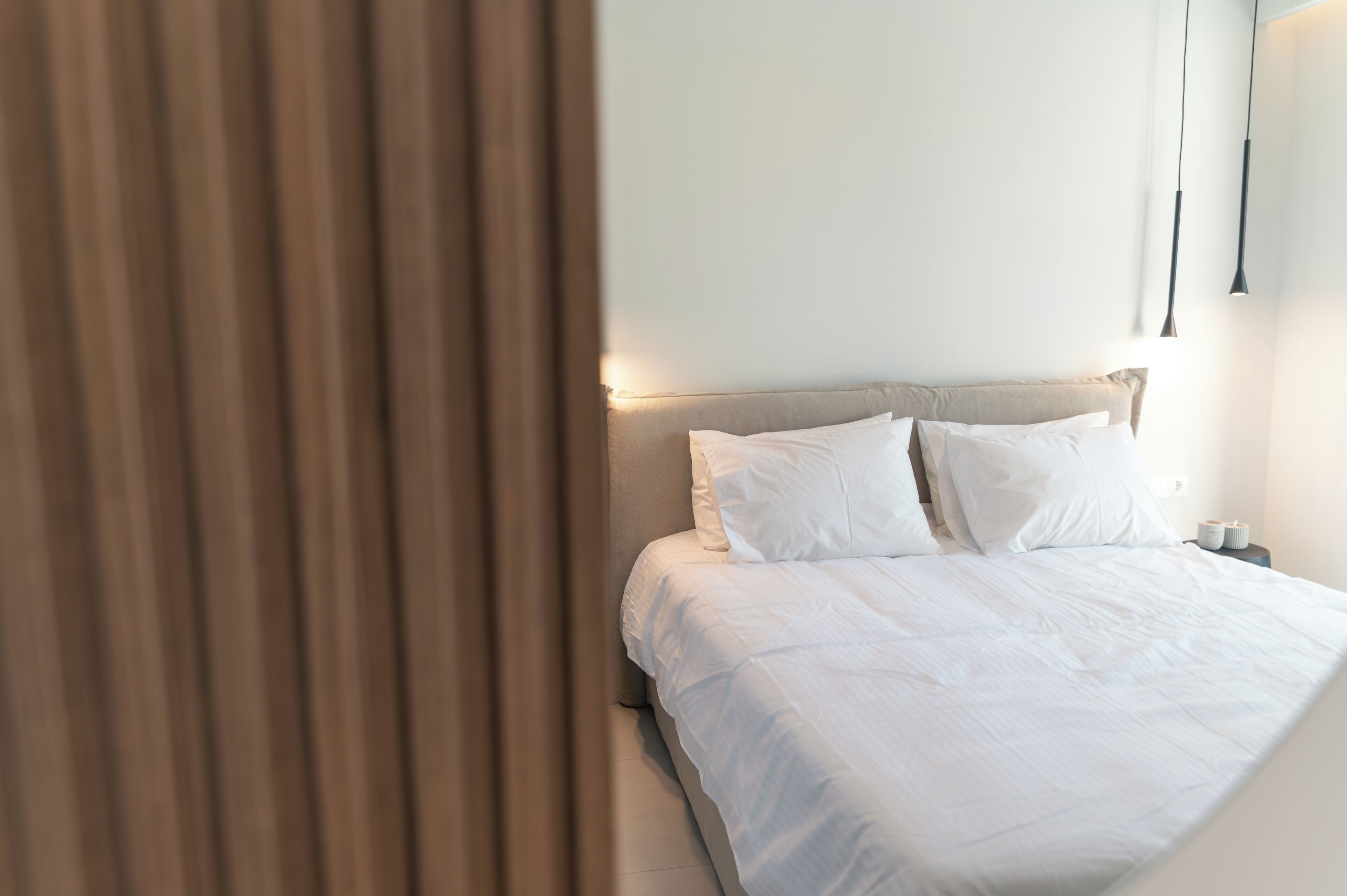 A neatly made bed with white linens, a headboard, and a bedside table with a lamp.