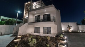 A modern two-story building with a balcony, large windows, and a well-lit exterior.