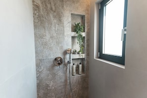 Ein Badezimmer mit Dusche, einem Fenster und einem Ablagefach mit Pflegeprodukten.