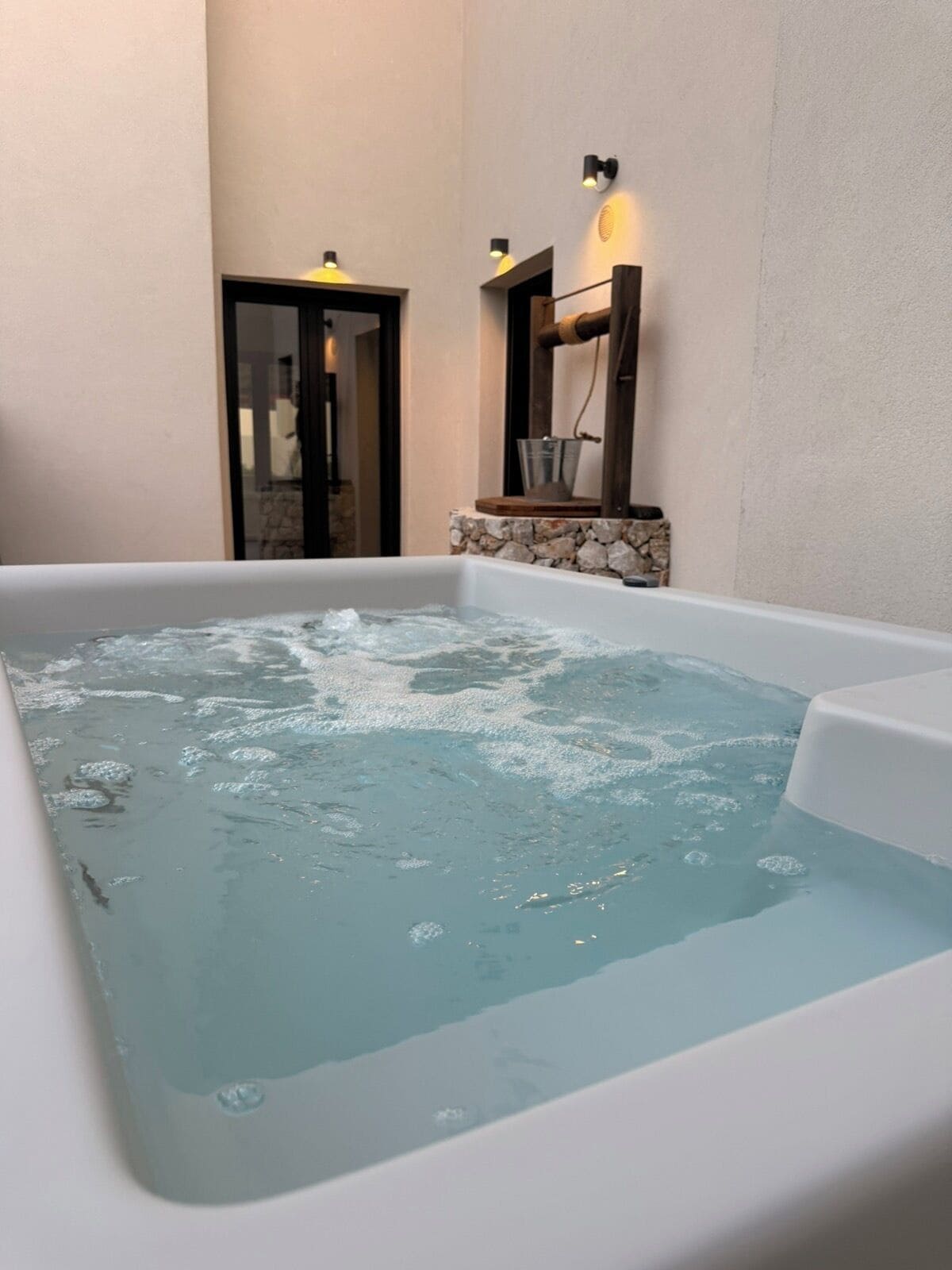 A hot tub with water, a stone wall, and a door.