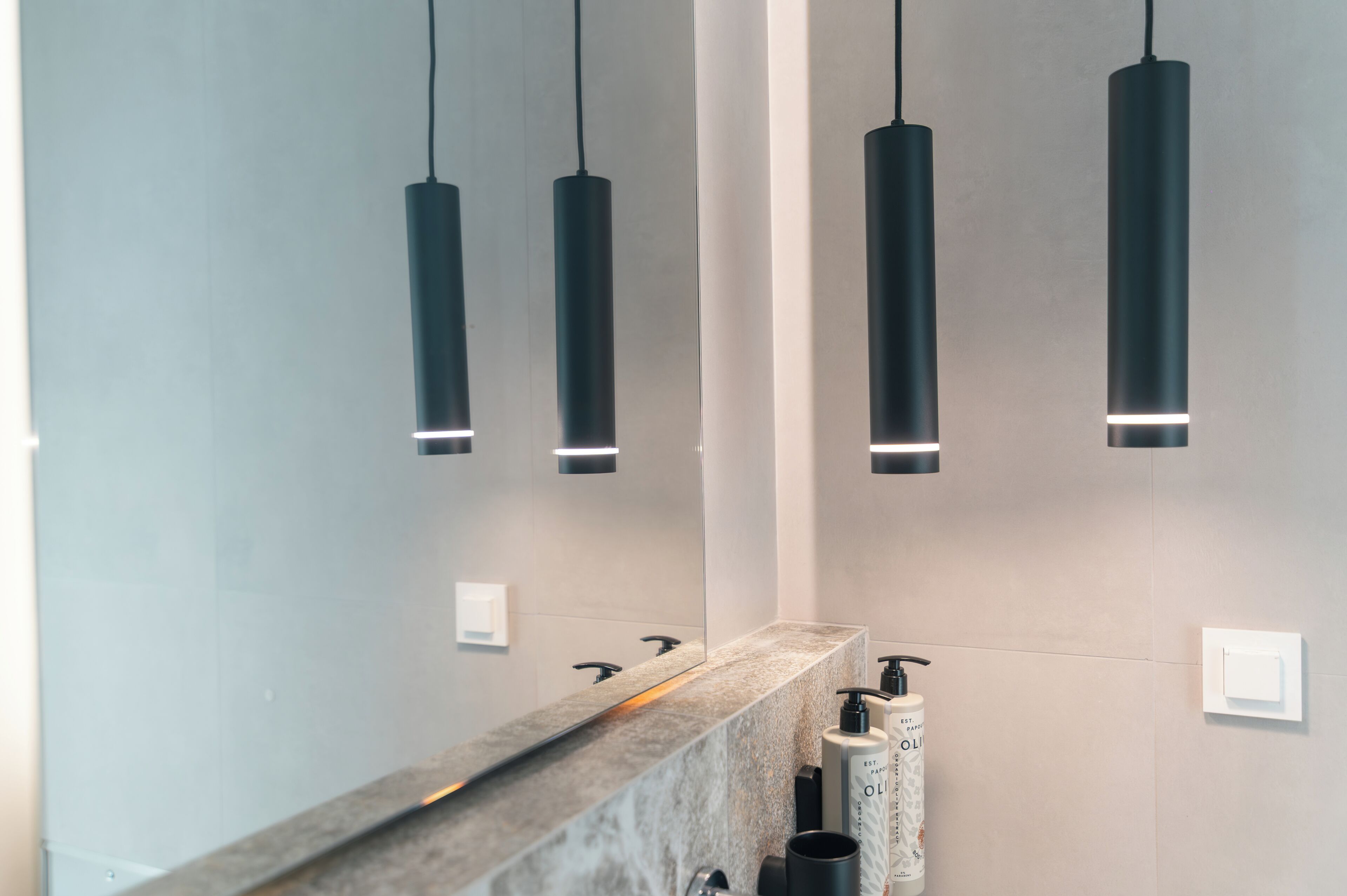 Een moderne badkamer met een marmeren aanrechtblad, zwarte hanglampen en een grote spiegel.