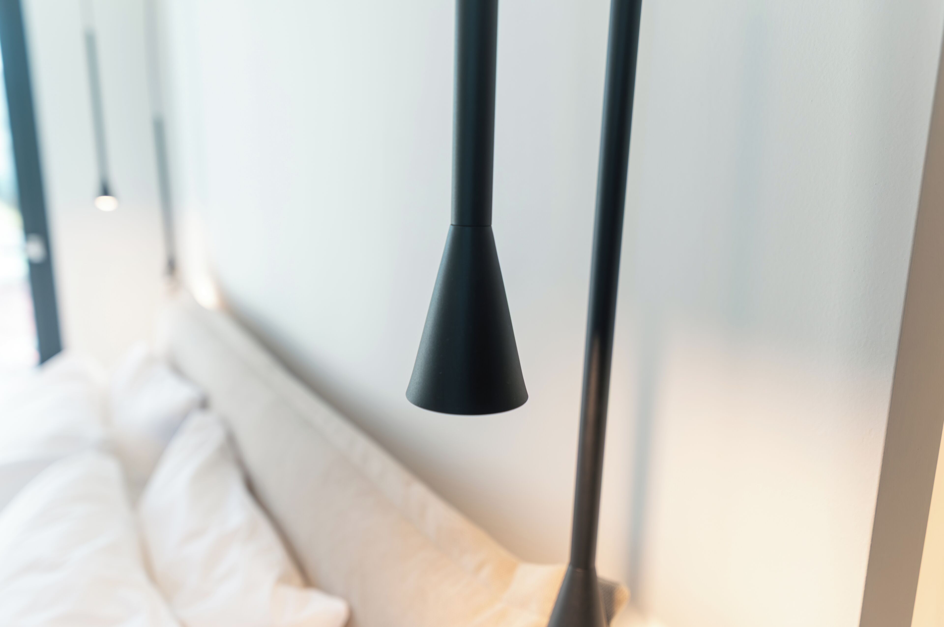 A bed with white linens and a black lamp.