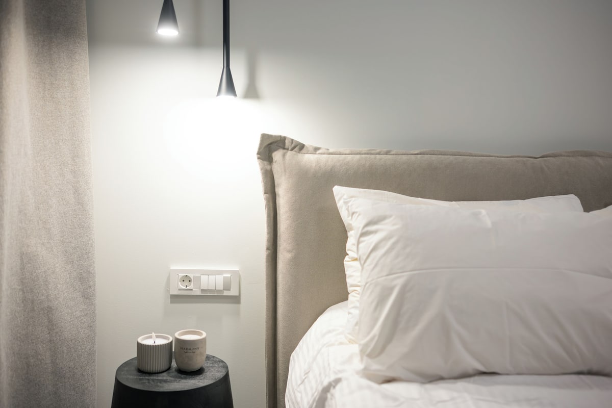 Een slaapkamer met een bed, een nachtkastje met twee kaarsen, een stopcontact en een hanglamp.