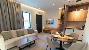 A modern living room with a sofa, coffee table, dining table set for four, and a kitchen area with wooden cabinets.