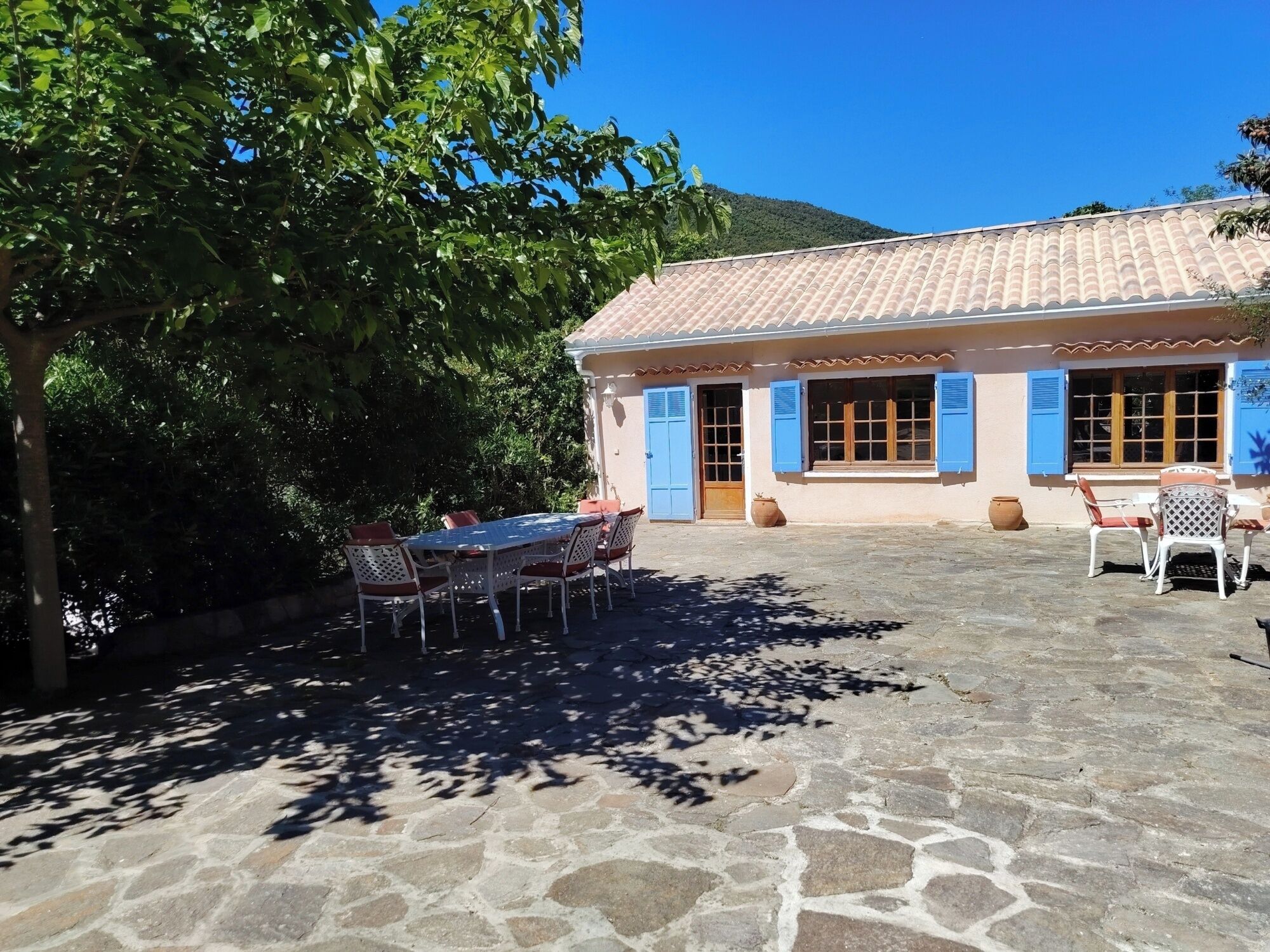 A building with a tiled roof, a patio with stone flooring, and a table with chairs.