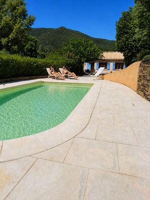 Ein Swimmingpool mit klarem Wasser, umgeben von Steinfliesen und zwei Liegestühlen.