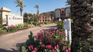 Entrada de un hotel con un letrero que dice "Azure", rodeada de palmeras y flores.