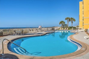 A pool with a clear view of the ocean, surrounded by lounge chairs and a yellow building. - 🌊Gulf Views | FREE Beach Svc | Pools+Splash Pad | Azure 323🌊 (Fort Walton Beach)