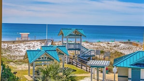 Un resort frente a la playa con una torre de salvavidas, cabañas de playa y un paseo marítimo que conduce al océano.