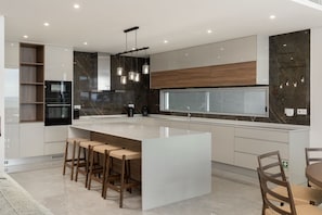 A modern kitchen with a large island, bar stools, and a window. - Premium villa on the seafront in Madalena|BayShore (Madalena do Mar)