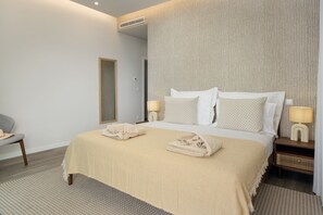 A neatly arranged hotel room with a large bed, two bedside tables with lamps, a chair, and a textured wall. - Premium villa on the seafront in Madalena|BayShore (Madalena do Mar)