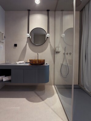 A modern bathroom with a round mirror, a vessel sink, a handheld showerhead, and a glass-enclosed shower. - Moon & Sun Funchal (Funchal)