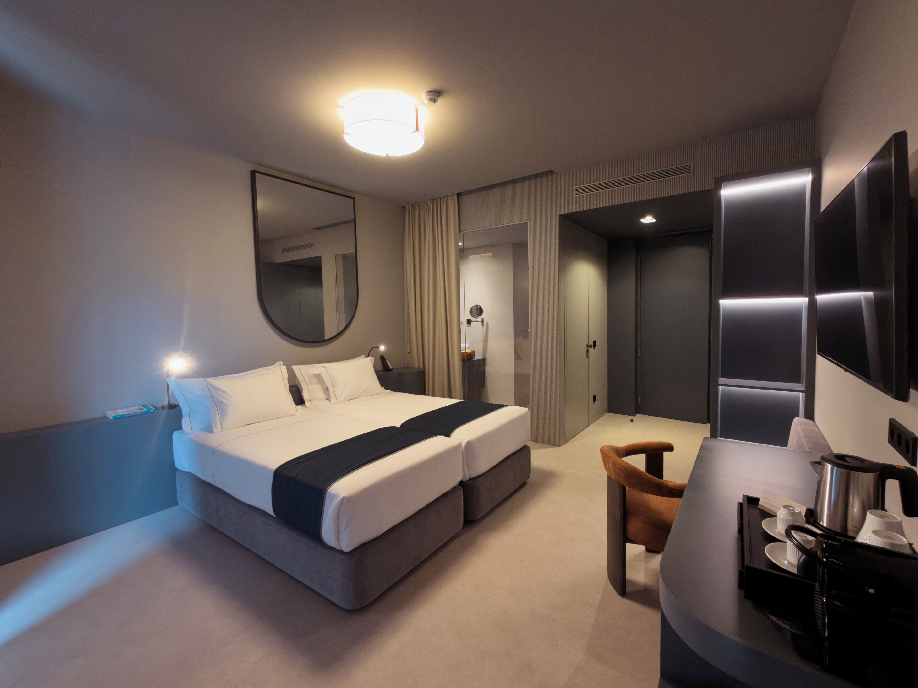 Et moderne hotelværelse med en stor seng, et skrivebord med kaffemaskine, et spejl og et fjernsyn.
