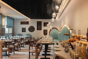 A restaurant interior with multiple dining tables, chairs, and a variety of food items displayed on the counter. - Moon & Sun Funchal (Funchal)