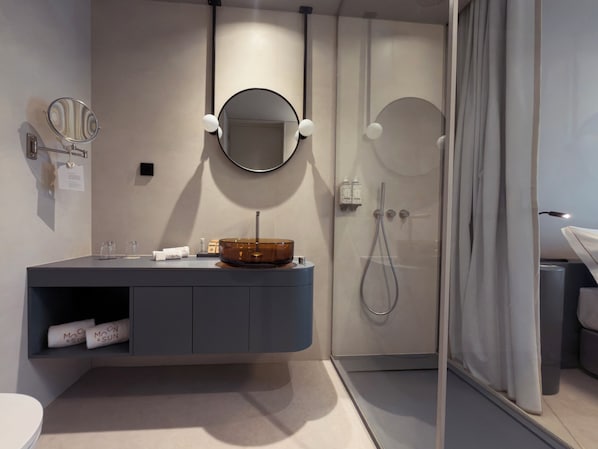 A modern bathroom with a round mirror, a round sink, a shower, and a glass partition.