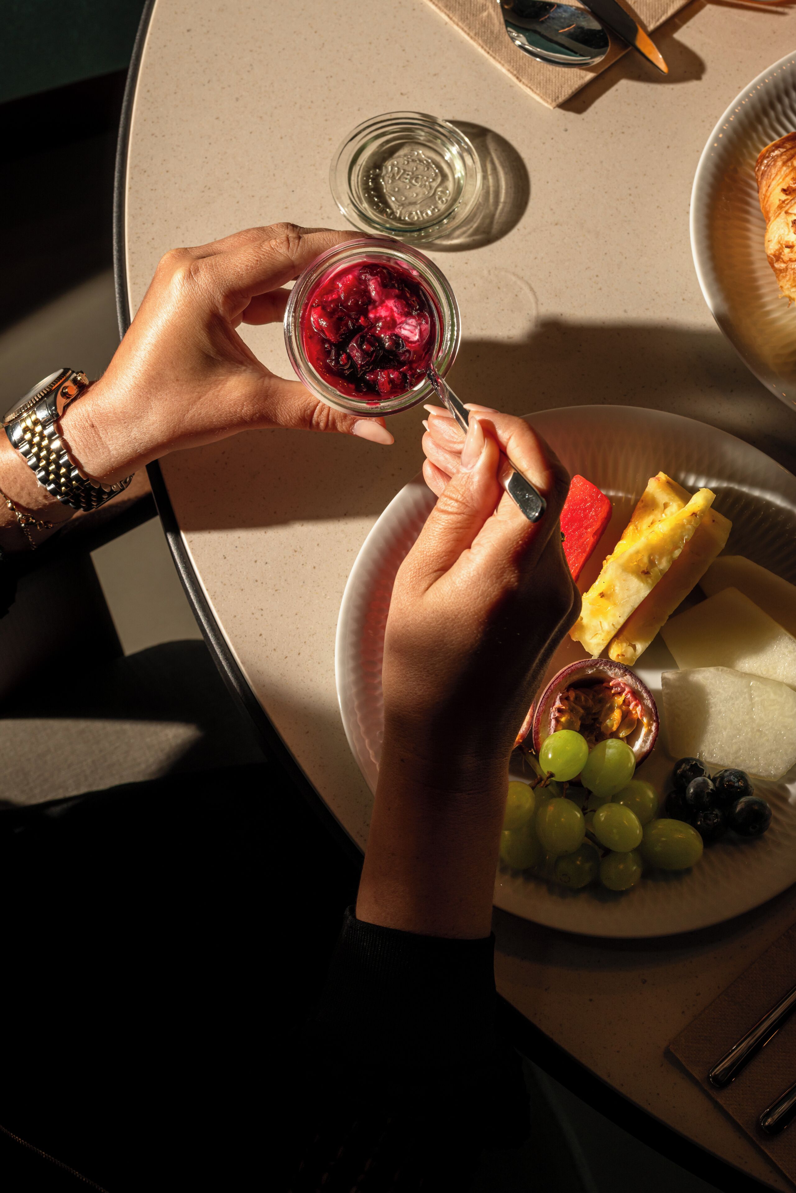 A table with a plate of fruit, a glass of red drink, and a slice of bread.