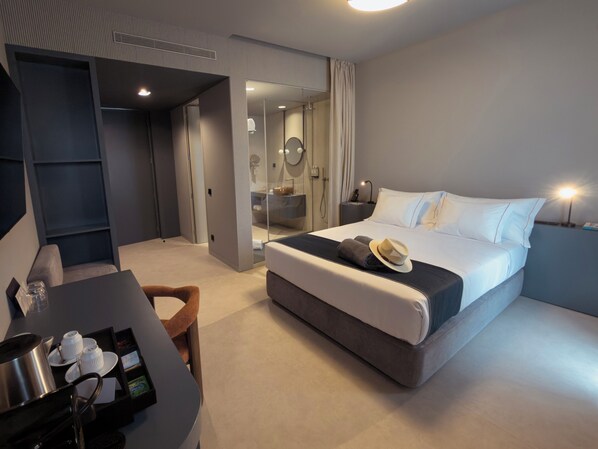 A modern hotel room with a large bed, a desk with a tray of breakfast items, a shower area, and a mirror.