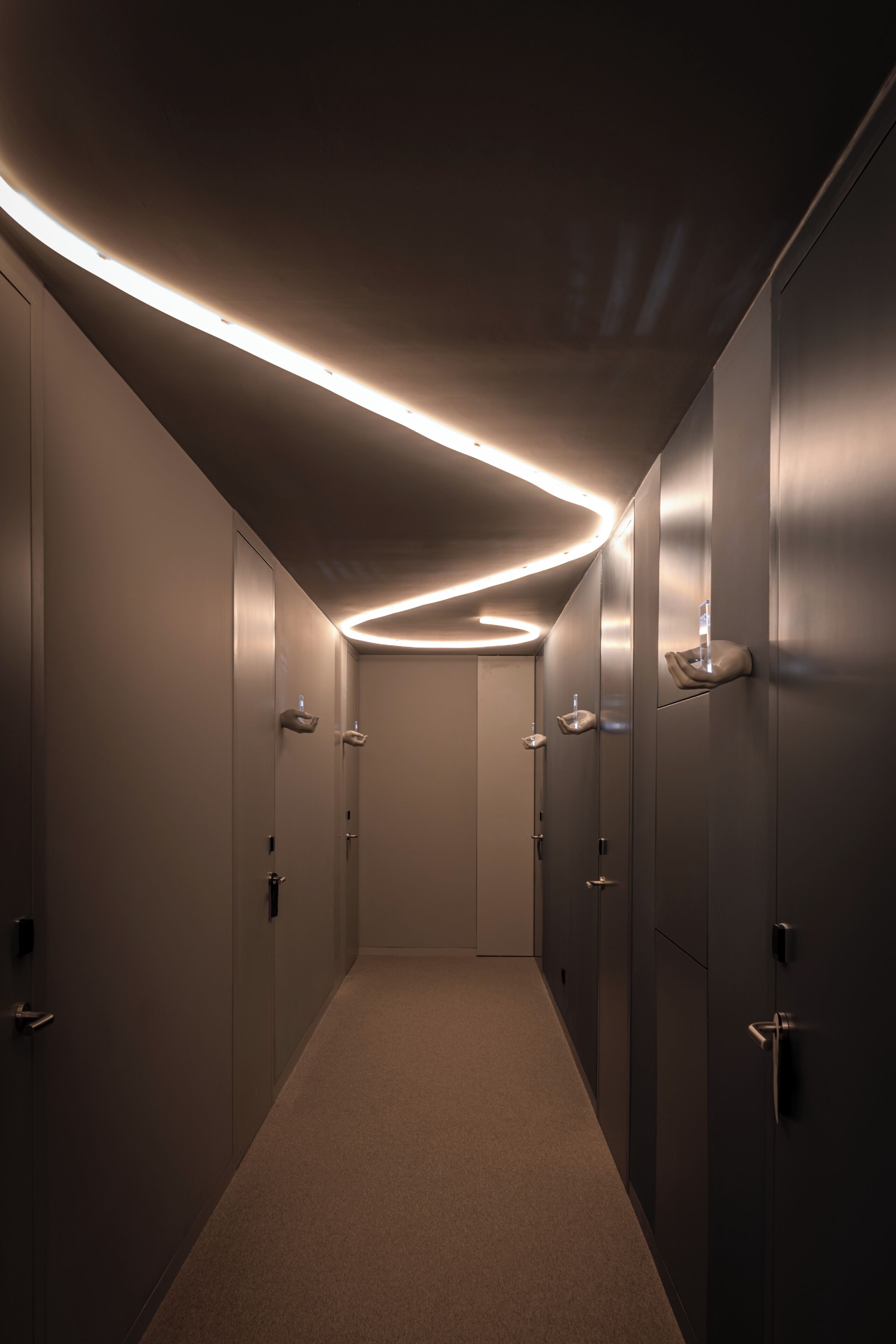 Un couloir au design moderne, caractérisé par un tracé rectiligne, un éclairage encastré et un revêtement de sol en moquette.
