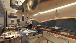 Un interior de restaurante moderno con mesas redondas, asientos azules y un camarero atendiendo.