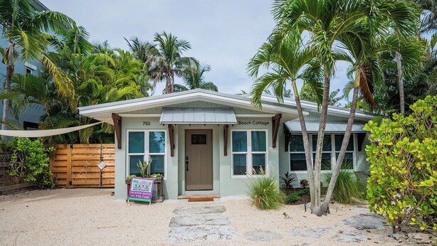 A beachfront cottage with a number 750 sign, a sandy driveway, and palm trees. - Zen Beach Cottage: Beautiful ground level home steps to beach (Anna Maria)