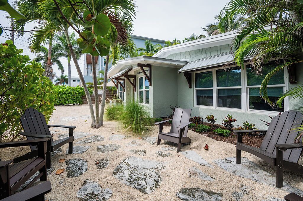 A beachfront property with a covered patio, outdoor seating, and tropical vegetation.