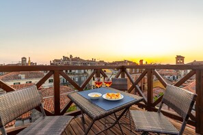 A balcony with wicker furniture, a table with a plate of food and two glasses of red wine, and a cityscape view in the background. - Bright Top-Floor Retreat with Panoramic Terrace in the Heart of Venice (Venice)