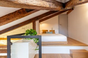 A bedroom with a sloped ceiling, wooden beams, a bed with pillows, a bedside table, and a potted plant. - Bright Top-Floor Retreat with Panoramic Terrace in the Heart of Venice (Venice)