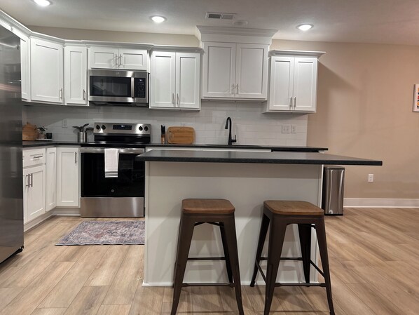 A modern kitchen with white cabinets, stainless steel appliances, a black countertop, and two wooden stools. - 
Blue nest - Awesome 3-bedroom bungalow with AC in charming Elizabethtown (Elizabethtown)