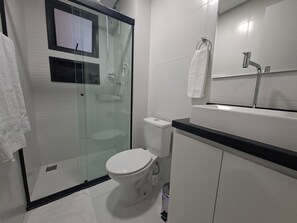 A modern bathroom with a glass-enclosed shower, a toilet, a sink with a mirror, and a towel rack. - Estúdio e lazer completo piscina rooftop (São Paulo)