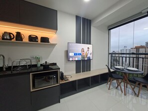 A modern kitchen with a TV, a dining area with a table and chairs, and a balcony with a city view. - Estúdio e lazer completo piscina rooftop (São Paulo)