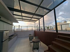 A modern balcony with a glass ceiling, a dining area with chairs, and a view of the city skyline. - Estúdio e lazer completo piscina rooftop (São Paulo)
