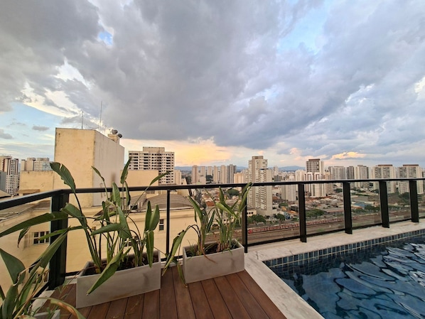 A rooftop pool with a city view, potted plants, and a metal railing. - Estúdio e lazer completo piscina rooftop (São Paulo)