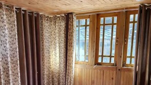 A wooden-paneled room with a bed, curtains, and windows. - Divine Home stay  (Rajgarhi)