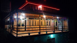 A wooden building with a balcony, potted plants, and string lights. - Divine Home stay  (Rajgarhi)