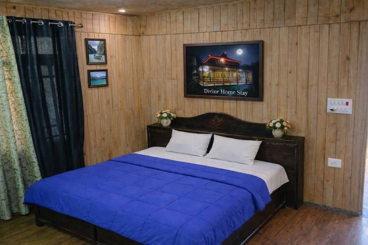 A bedroom with a wooden paneled wall, a bed with a blue bedspread, two framed pictures, and a sign above the bed.