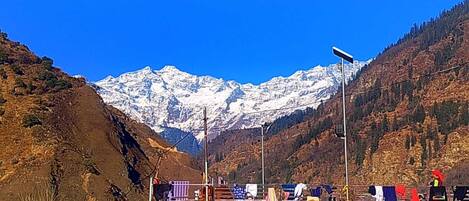 A mountainous landscape with a snow-capped peak in the background, a fence with hanging laundry, and a streetlight.