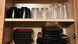Ett träskåp med hyllor som innehåller svarta muggar, genomskinliga glas och staplade svarta tallrikar.