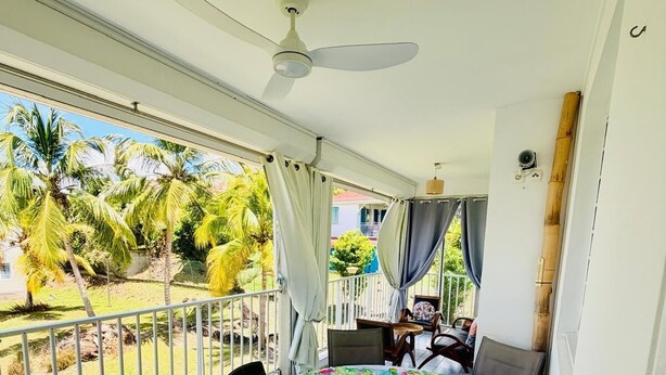 A balcony with a table and chairs, a ceiling fan, and a view of palm trees. - Spacious T3 400m from Anse à l'Ane beach (Les Trois Ilets) (Les Trois-Îlets)