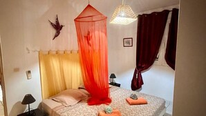 A bedroom with a bed, a bedside table, a lamp, a hanging light fixture, and a window with curtains. - Spacious T3 400m from Anse à l'Ane beach (Les Trois Ilets) (Les Trois-Îlets)