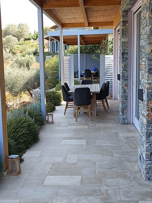 Ein überdachter Patio-Bereich mit Steinboden, einem Holztisch und Stühlen sowie einer Steinwand.