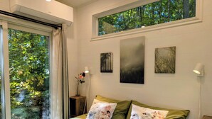 Een slaapkamer met een bed, een nachtkastje, een raam met uitzicht op bomen en kunstwerken aan de muur.